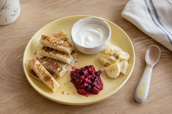 A simple breakfast with pancake strips, yogurt, soft fruit, and a child-sized spoon