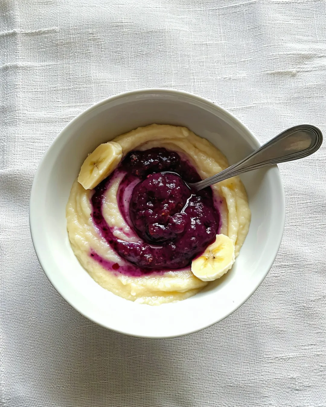Mashed banana swirled with smashed blueberry in a small white bowl