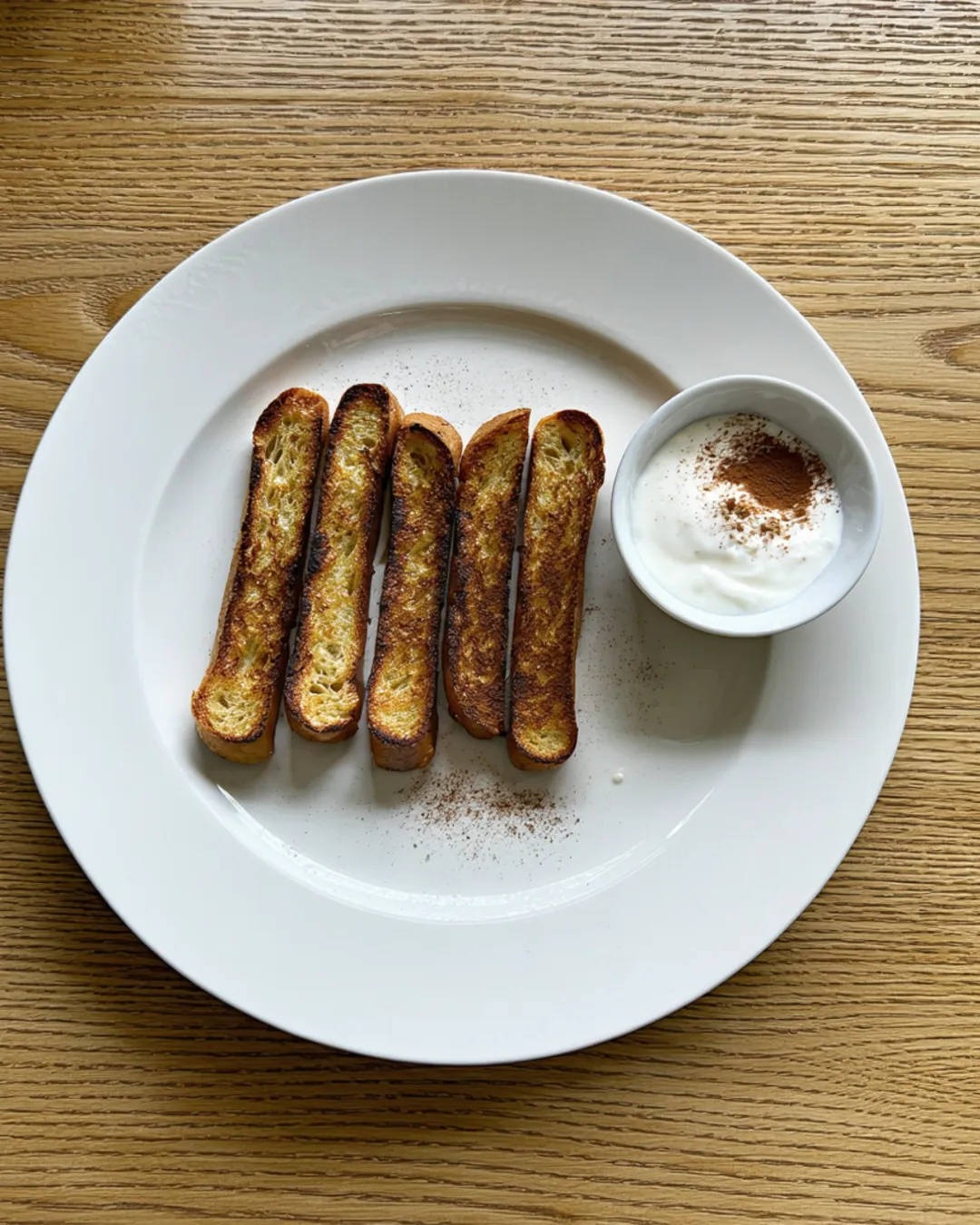 Golden French toast sticks with a small bowl of yogurt for dipping